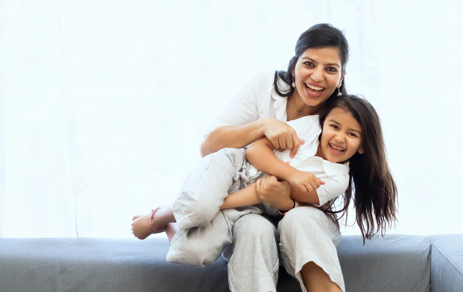 A mother and daughter laughing together on a sofa at home